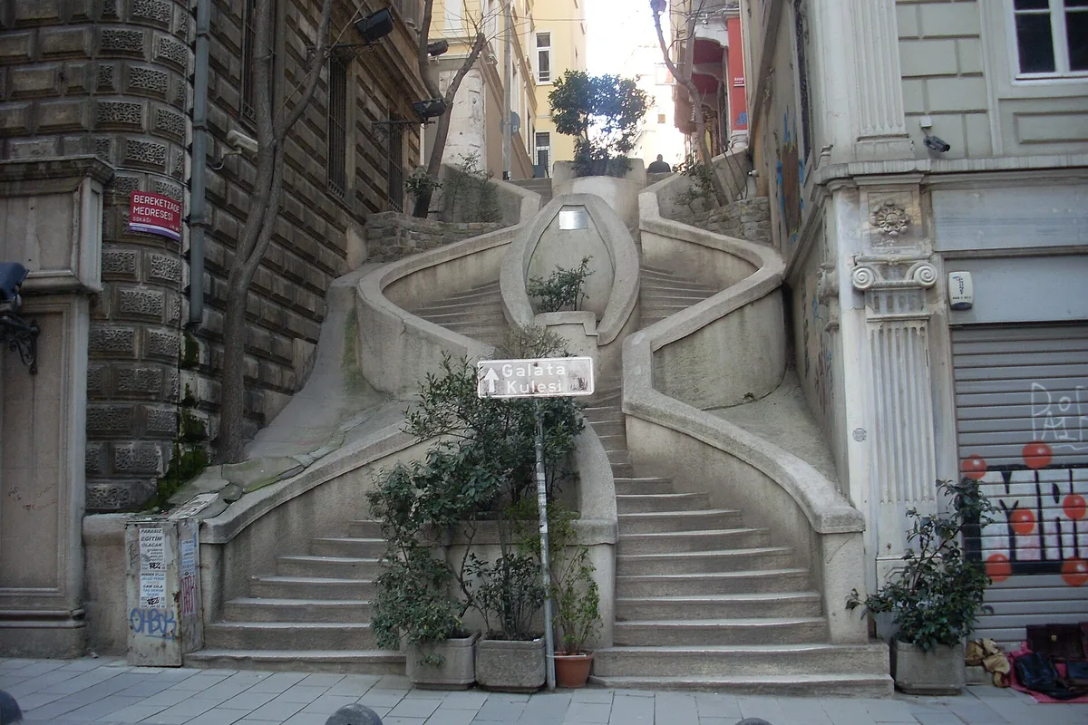 The curving twin flights of the Camondo Stairs in Galata, with a stone balustrade and potted plants.