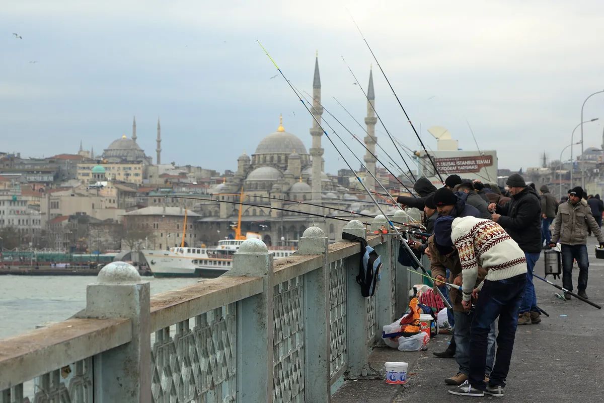 Fishermen along the railing of the Galata Bridge, with the domes and minarets of the old city behind them.
