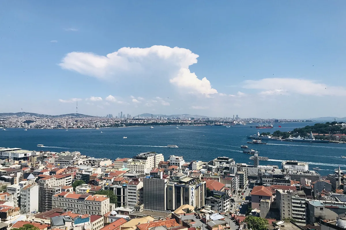 The view over Beyoğlu rooftops to the Golden Horn, the Bosphorus and the far shore under a cloudy blue sky.